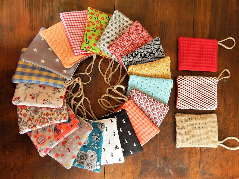 May include: A collection of 16 colorful fabric pouches with different patterns, arranged in a circle on a wooden surface. Each pouch has a drawstring closure and a small loop for hanging.