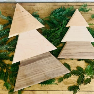 May include: Two wooden Christmas tree ornaments, one larger than the other. The larger tree is made of three layers of wood, with the top layer being light brown, the middle layer being a lighter shade of brown, and the bottom layer being a darker shade of brown. The smaller tree is made of three layers of wood, with the top layer being a light brown, the middle layer being a white, and the bottom layer being a darker shade of brown.