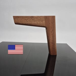 May include: A single L-shaped furniture leg crafted from dark brown wood with a visible natural grain pattern. The leg features a horizontal mounting section and a vertical support post, showcasing a smooth, polished finish throughout the piece.