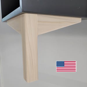 May include: Close-up of a light wood furniture leg with a square shape. The leg is attached to a black surface.