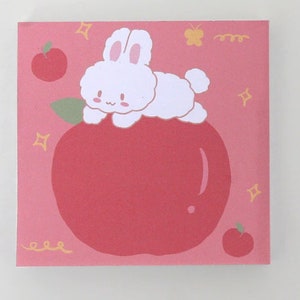 Pode incluir: Um fundo rosa com um coelho branco sentado em uma ma&ccedil;&atilde; vermelha. O coelho tem uma cauda fofa e est&aacute; olhando para a esquerda. H&aacute; pequenas estrelas amarelas e uma borboleta amarela no fundo.