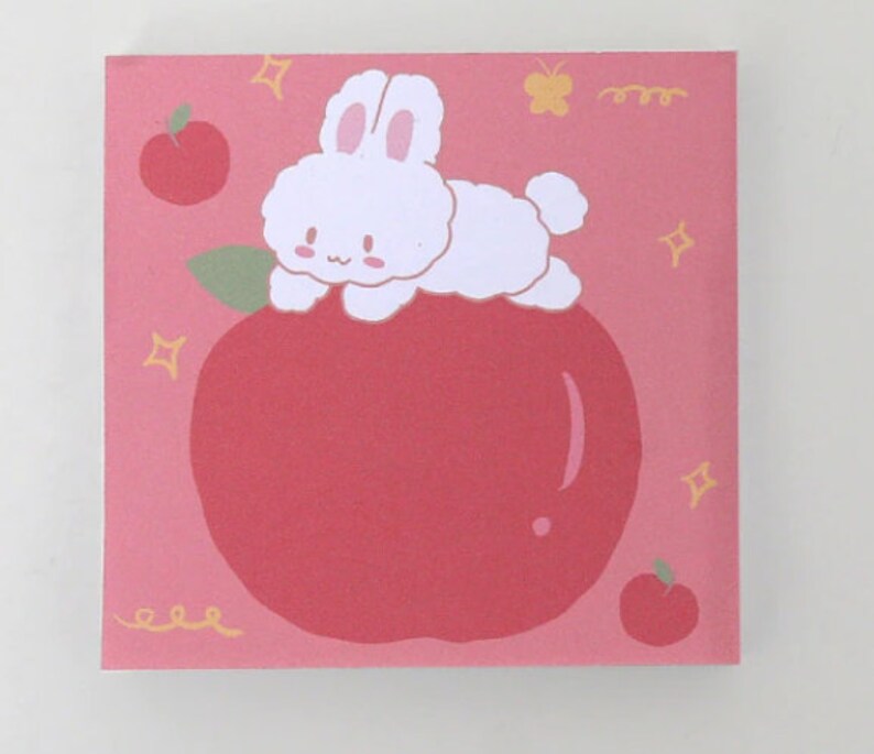 Pode incluir: Um fundo rosa com um coelho branco sentado em uma ma&ccedil;&atilde; vermelha. O coelho tem uma cauda fofa e est&aacute; olhando para a esquerda. H&aacute; pequenas estrelas amarelas e uma borboleta amarela no fundo.