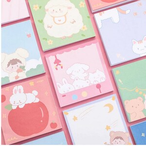 Pode incluir: Um conjunto de notas adesivas quadradas coloridas com v&aacute;rias ilustra&ccedil;&otilde;es de animais fofinhos. As notas apresentam uma ovelha, um gato, um coelho, um urso e uma menina usando um chap&eacute;u de urso. As notas s&atilde;o perfeitas para adicionar um toque de fantasia ao seu planejador, di&aacute;rio ou mesa.