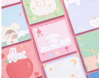Puede incluir: Un conjunto de notas adhesivas cuadradas de colores con varias ilustraciones de animales lindos. Las notas presentan una oveja, un gato, un conejito, un oso y una niña con un gorro de oso. Las notas son perfectas para agregar un toque de fantasía a tu planificador, diario o escritorio.