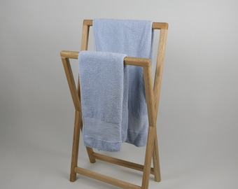 May include: A light wood towel rack with two light blue towels. The rack has an X-frame design and is made of natural-colored wood. The towels are folded over the top bars.