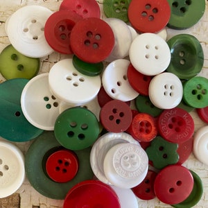 May include: A collection of assorted round buttons in shades of red, white, and green. The buttons vary in size and feature either two or four holes for attachment. Some buttons have embossed text including the words Exclusive Too and Karrimor.