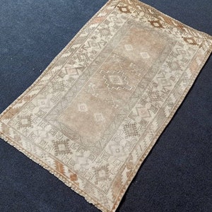 May include: A beige and brown patterned rug with a fringed edge. The rug has a geometric design with a central diamond shape.