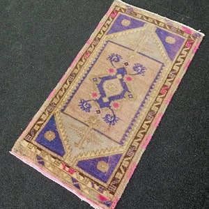 May include: A small, rectangular rug with a pink, brown, and blue geometric pattern. The rug has a fringe border.