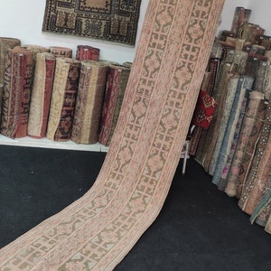 May include: A long, narrow, pink and brown patterned rug with a geometric design. The rug is folded in half and leaning against a wall.