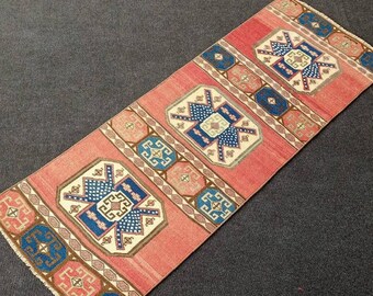 May include: A red, blue, and white patterned runner rug with a geometric design. The rug has a fringe border.