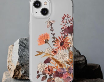 Puede incluir: Una funda transparente para teléfono con un diseño floral con flores secas en tonos naranja, rojo y marrón. La funda tiene un recorte para la lente de la cámara.