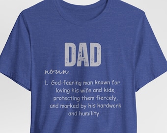 Puede incluir: Una camiseta azul con un gráfico blanco que dice "DAD" y define la palabra como un "hombre temeroso de Dios conocido por amar a su esposa e hijos, protegerlos ferozmente y marcado por su trabajo duro y humildad."