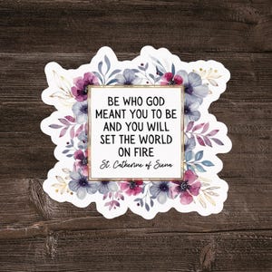 Puede incluir: Una pegatina con un diseño floral y la cita "SÉ QUIEN DIOS QUERÍA QUE FUERAS Y PRENDERÁS FUEGO AL MUNDO" atribuida a Santa Catalina de Siena. La pegatina presenta flores moradas y azules con hojas verdes.