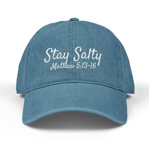 Puede incluir: Gorra de béisbol azul con la inscripción blanca "Stay Salty" en cursiva. Debajo está "Matthew 5:13-16". La gorra tiene una visera curva y un cierre de correa. El sombrero es de color azul claro.