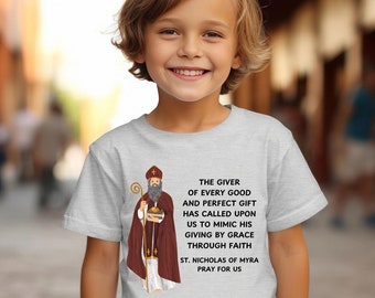May include: A light gray t-shirt with a graphic of Saint Nicholas of Myra, a Christian saint, holding a staff and wearing a red and gold robe. The text on the shirt reads: "The giver of every good and perfect gift has called upon us to mimic his giving by grace through faith. St. Nicholas of Myra pray for us."