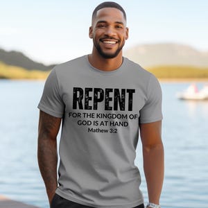 Könnte beinhalten: Ein graues T-Shirt mit dem Text "Repent for the kingdom of God is at hand Matthew 3:2" in Schwarz gedruckt.
