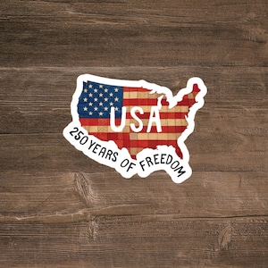 Puede incluir: Una pegatina troquelada con la forma del mapa de los Estados Unidos que presenta un patrón de bandera roja, blanca y azul con una textura desgastada. El texto USA está impreso en blanco y 250 YEARS OF FREEDOM en negro en la parte inferior.