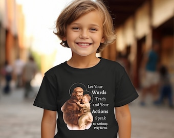 Puede incluir: Camiseta negra con un gráfico de San Antonio de Padua sosteniendo un bebé. El texto en la camiseta dice "Deja que tus palabras enseñen y tus acciones hablen. San Antonio, reza por nosotros."