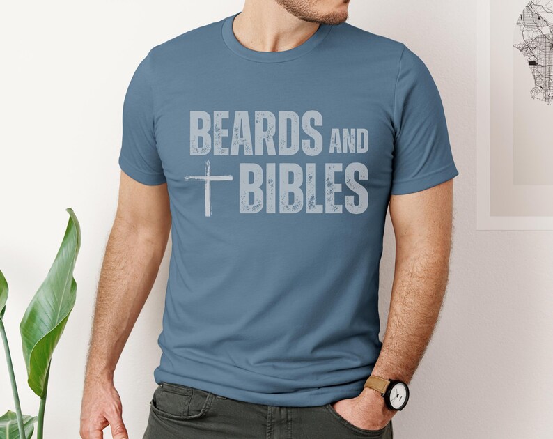 May include: A blue crew neck t-shirt with the text "BEARDS and BIBLES" in a distressed, light grey font. A white cross is centered below the word "BEARDS". The shirt is made of a soft material.