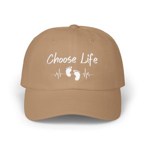 May include: A tan baseball cap with the words "Choose Life" embroidered in white. The design includes a heartbeat line with two baby footprints. The cap is made of a soft, durable material.