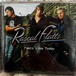 May include: A CD case with a photo of three men, a band called Rascal Flatts, with the album title "Feels Like Today".