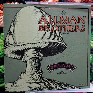 K&ouml;nnte beinhalten: Eine CD-H&uuml;lle des Albums "Dreams" von The Allman Brothers Band. Das Cover zeigt eine gro&szlig;e Pilzillustration in Gr&uuml;n- und Schwarzt&ouml;nen, mit dem Bandnamen in orangefarbenen Buchstaben. Der Albumtitel ist ebenfalls abgebildet.