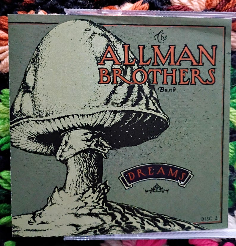 K&ouml;nnte beinhalten: Eine CD-H&uuml;lle des Albums "Dreams" von The Allman Brothers Band. Das Cover zeigt eine gro&szlig;e Pilzillustration in Gr&uuml;n- und Schwarzt&ouml;nen, mit dem Bandnamen in orangefarbenen Buchstaben. Der Albumtitel ist ebenfalls abgebildet.