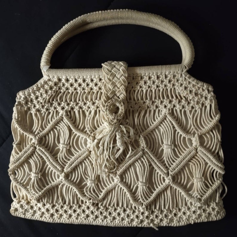 May include: A cream-coloured crocheted handbag with a knotted handle and a tassel detail.
