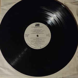 Puede incluir: Disco de vinilo negro con una etiqueta blanca. La etiqueta tiene el texto "Emerson Lake & Palmer Works Volume 2" y enumera los t&iacute;tulos de las canciones "So Far to Fall", "Maple Leaf Rag", "I Believe in Father Christmas", "Close But Not Touching", "Honky Tonk Train Blues" y "Show Me the Way to Go Home".