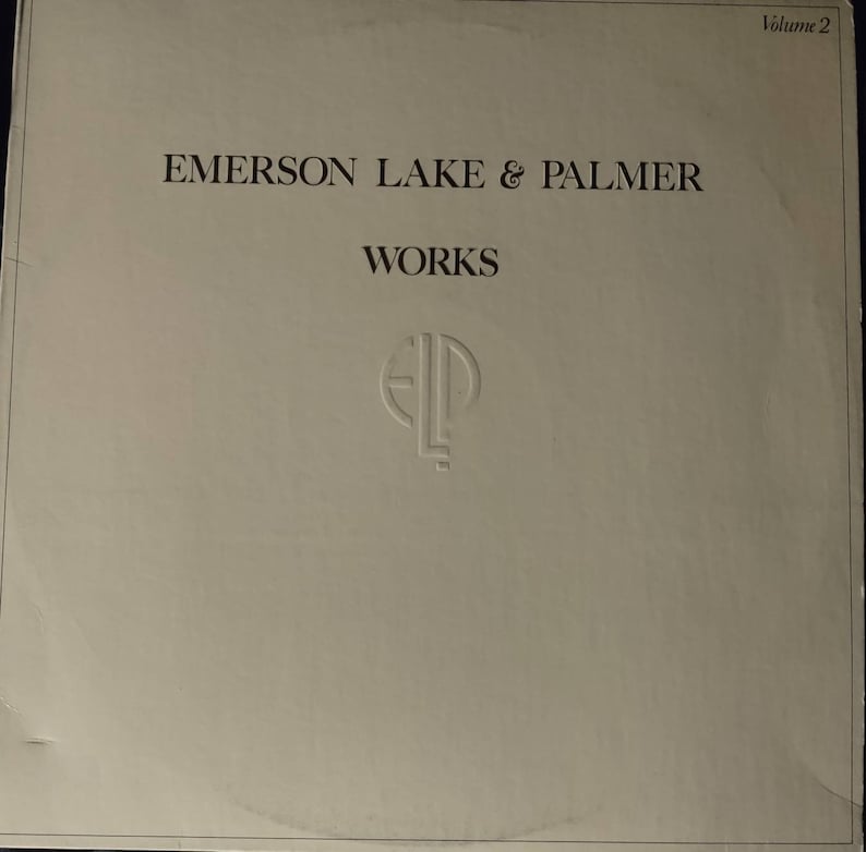 Puede incluir: Una portada de &aacute;lbum de vinilo blanco con el texto "Emerson Lake & Palmer" y "Works" en negro. La portada del &aacute;lbum tambi&eacute;n presenta el logotipo de la banda, "ELP", en un c&iacute;rculo.
