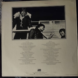 Puede incluir: La contraportada de un &aacute;lbum de vinilo con una foto de tres hombres. El &aacute;lbum se titula "Emerson, Lake & Palmer". La lista de canciones de cada lado del disco est&aacute; impresa en la contraportada.