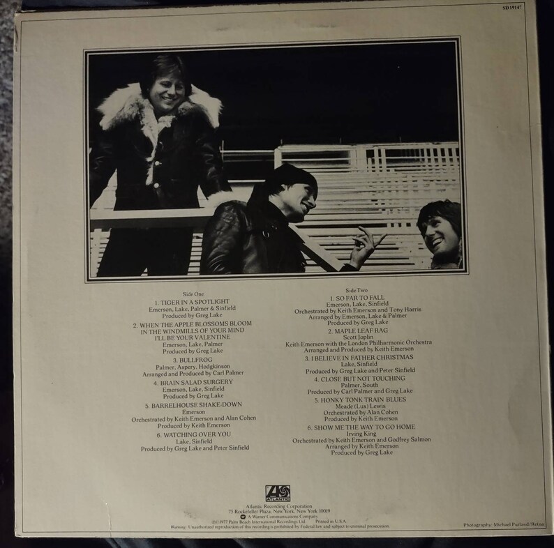 Puede incluir: La contraportada de un &aacute;lbum de vinilo con una foto de tres hombres. El &aacute;lbum se titula "Emerson, Lake & Palmer". La lista de canciones de cada lado del disco est&aacute; impresa en la contraportada.