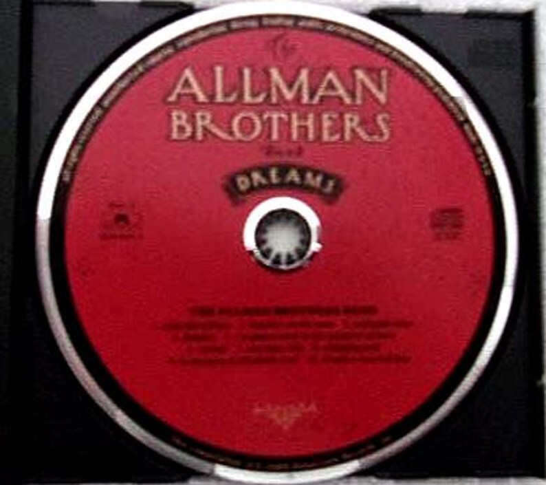 K&ouml;nnte beinhalten: Eine CD mit roter Oberfl&auml;che, auf der der Text "ALLMAN BROTHERS" und "DREAMS" in einer Serifenschrift steht. Die Disc befindet sich in einer schwarzen H&uuml;lle. Sie hat einen silbernen Rand und eine silberne Mitte.
