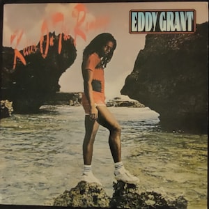 May include: A man with long dreadlocks stands on a rock in the ocean. He is wearing a red and white shirt, red shorts, and white sneakers. The album cover text reads "Killa On The Rampage" and "EDDY GRANT".