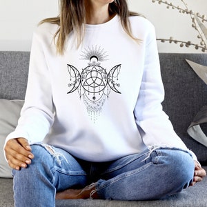 Könnte beinhalten: Weißer Pullover mit einem schwarz-weißen Grafikdesign eines dreifachen Mondes mit einem keltischen Knoten und floralen Akzenten.
