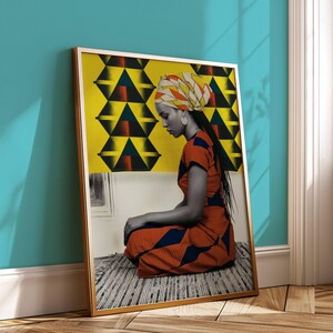 May include: A framed art print featuring a woman in a colorful patterned dress and head wrap, seated in front of a yellow and black geometric design. The artwork is displayed against a teal wall.