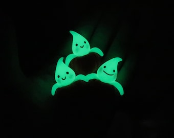 May include: Three glowing green ghost figurines with happy faces. The ghosts are arranged in a triangle shape.