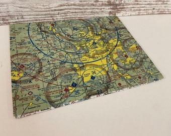May include: A square coaster featuring a detailed aviation sectional chart with yellow, blue, and green hues. The chart includes various symbols, numbers, and place names, such as Olathe and Johnson County.