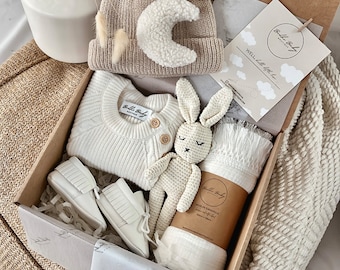 May include: A gift box containing a beige knit beanie with a white crescent moon patch, a white long-sleeve knit sweater with two wooden buttons, a pair of white leather moccasins, a crocheted rabbit toy, and a muslin swaddle with a 120cm x 120cm label.