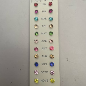 May include: A card with 12 pairs of colourful rhinestone earrings, each pair representing a month of the year. The card is white with black text and a price tag that reads "£19.99 Jewelry".