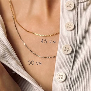May include: Two gold chains, one 45 cm and one 50 cm long, are shown on a model wearing a white shirt. The chains are delicate and have a simple design.
