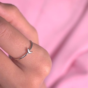 Könnte beinhalten: Ein silberner Ring mit einem Halbmond-Design. Der Ring wird an einem Finger getragen.