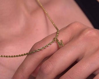 Może przedstawiać: Złoty naszyjnik z łańcuszkiem w kształcie liny z zawieszką w kształcie złotej litery 'N'.