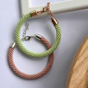 Pu&ograve; includere: Due braccialetti di perline, uno verde chiaro e uno rosa chiaro, con chiusure argentate e dorate.