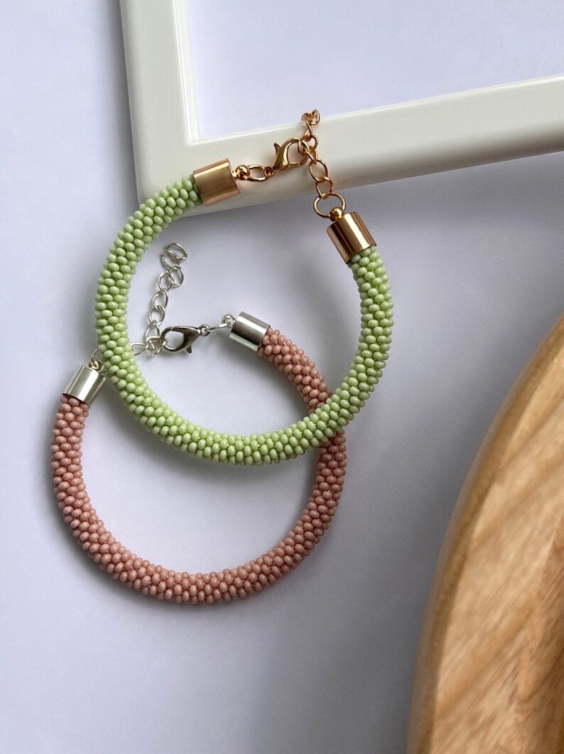 Pu&ograve; includere: Due braccialetti di perline, uno verde chiaro e uno rosa chiaro, con chiusure argentate e dorate.
