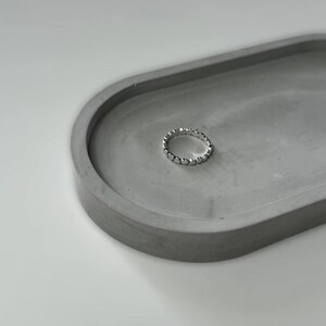 May include: A silver ring with a beaded design sits on a gray concrete dish.