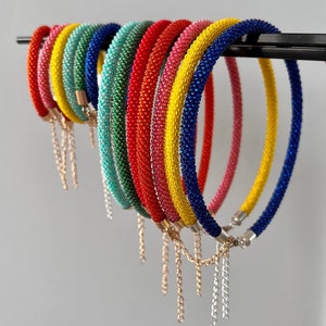 Pu&ograve; includere: Un set di braccialetti colorati con perline e dettagli di catena dorata e argentata. I braccialetti sono disposti a forma di arcobaleno, ogni braccialetto &egrave; di un colore diverso.