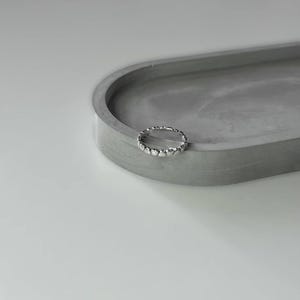 May include: A silver ring with a heart-shaped design. The ring is on a gray concrete surface.