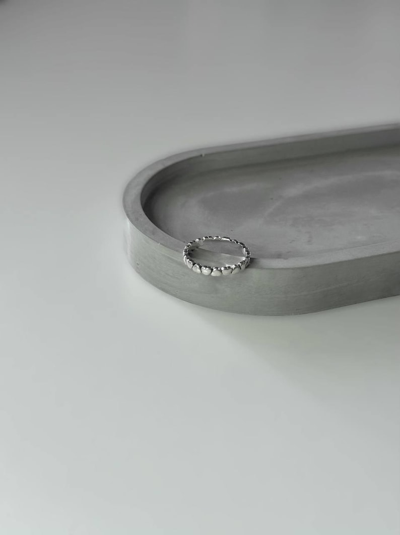 May include: A silver ring with a heart-shaped design. The ring is on a gray concrete surface.