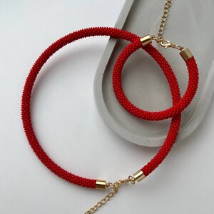 Pu&ograve; includere: Un set di collana e braccialetto di perline rosse con chiusure dorate. La collana &egrave; pi&ugrave; lunga del braccialetto.